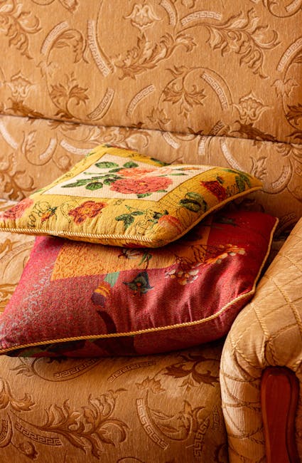 A white upholstered sofa with tufted backrest and rolled armrests is positioned against a white wall with decorative paneling in a well-lit living room. The sofa appears clean and well-maintained, wit